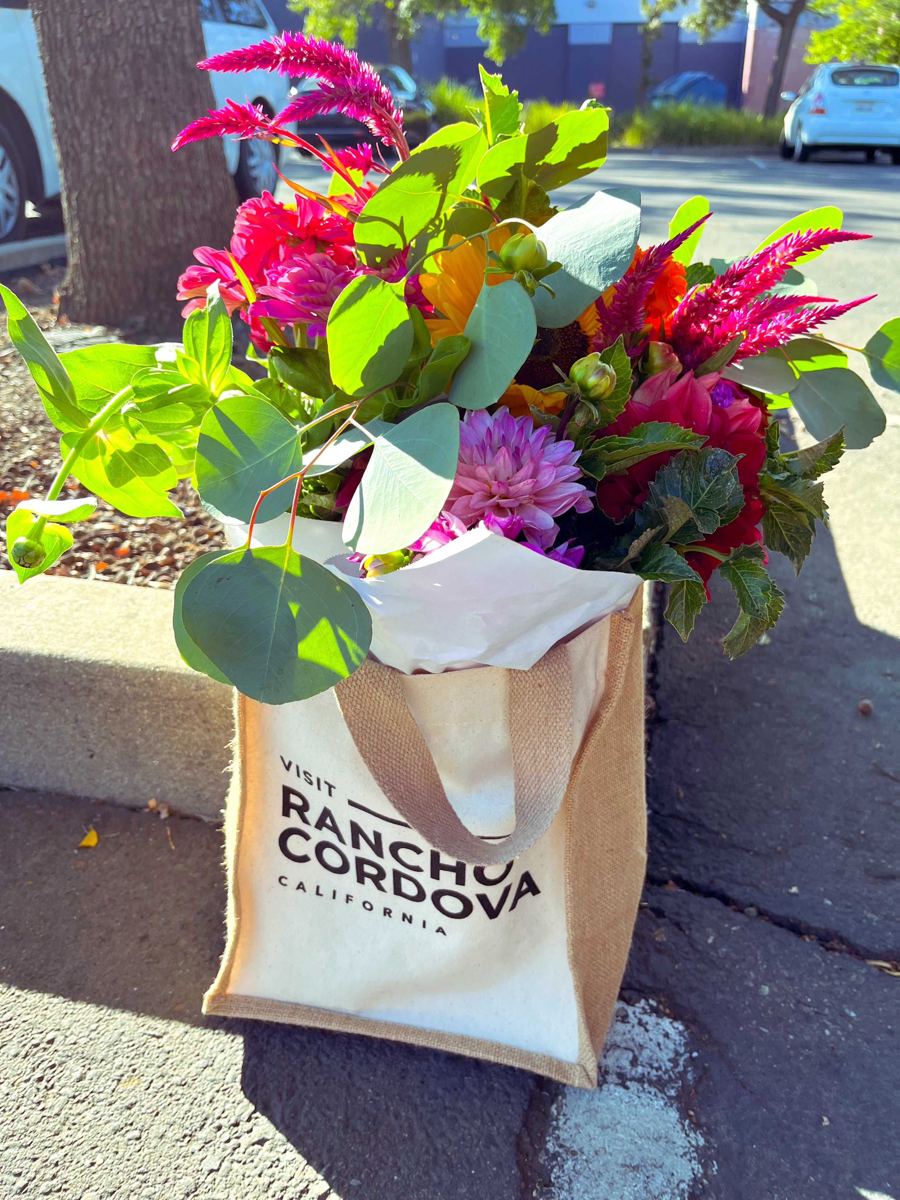 A Rancho Cordova branded tote bag filled with a bouquet from a local farmer's market